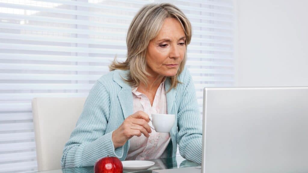 Mature woman working at her laptop holding a cup of coffee