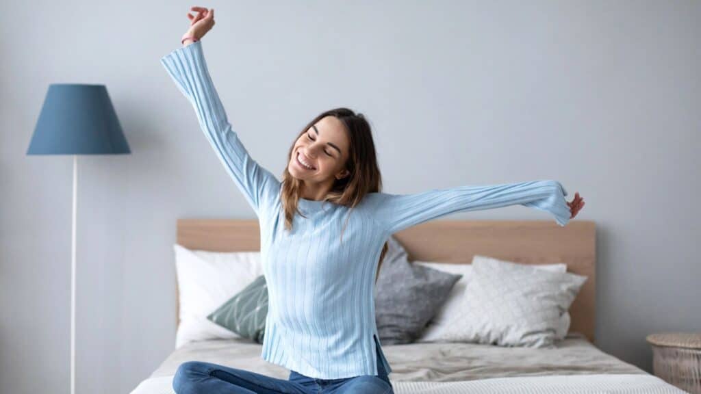 Woman sitting on bed with her arms up in the air looking happy